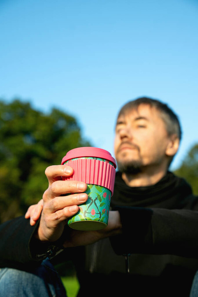 Одинокий, одинокий мужчина средних лет, пьющий кофе в парке. Концепция одиночества, социального дистанцирования и самовоспитания. Концепция психического здоровья, связанная с природой - Фото, изображение