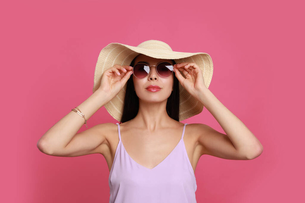 Beautiful young woman with straw hat and stylish sunglasses on pink background - Foto, immagini