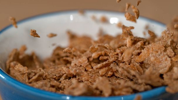 MACRO: Healthy whole grain breakfast cereal flakes fall into an empty bowl. - Photo, Image