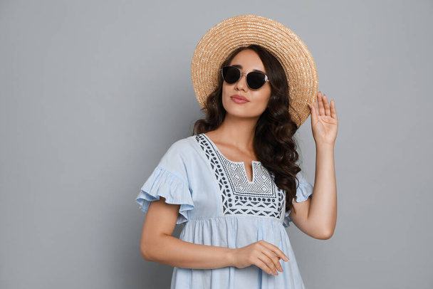 Beautiful young woman with straw hat and stylish sunglasses on light grey background - Fotó, kép