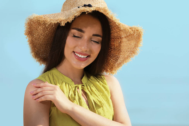 Beautiful young woman wearing straw hat on blurred background. Stylish headdress - Foto, afbeelding