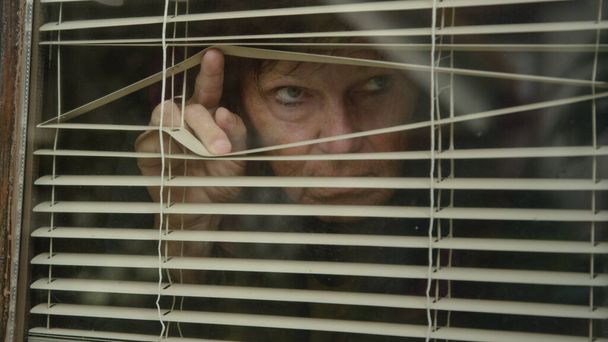 Κοντινό πλάνο: Φοβισμένη γυναίκα κοιτάζει έξω από το παράθυρό της, ενώ είναι κλειδωμένο κατά τη διάρκεια του ιού - Φωτογραφία, εικόνα