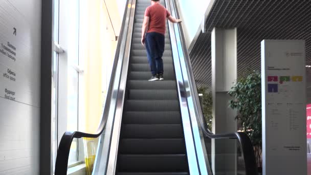 Человек в красной футболке поднимается по эскалатору в бизнес-центре. HDR. Молодой человек на эскалаторе в универмаге. - Кадры, видео
