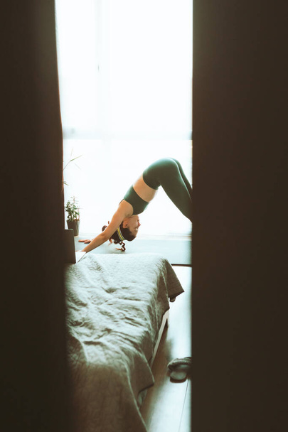 γυναίκα κάνει γιόγκα στο σπίτι κοντά σε μεγάλο παράθυρο υγιεινό τρόπο ζωής - Φωτογραφία, εικόνα
