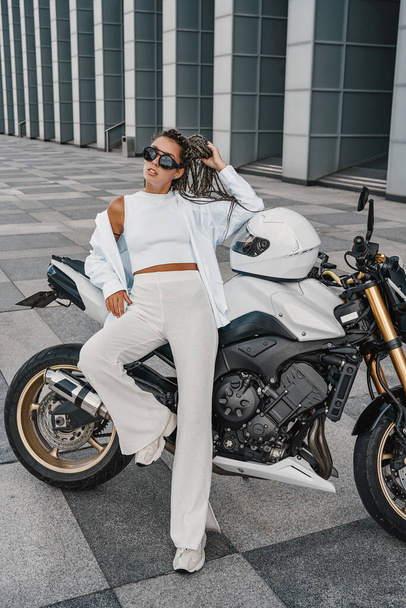 Shot of stylish woman biker leaning her motorcycle outside - Fotó, kép