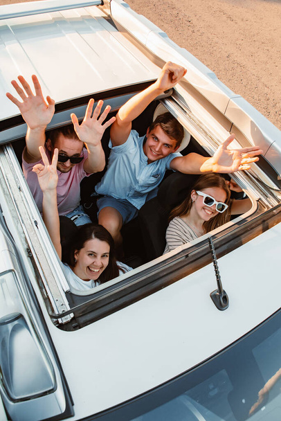 Bir grup arkadaş arabanın tepesinden yukarı bakıyor. Yolculuk. dostluk - Fotoğraf, Görsel