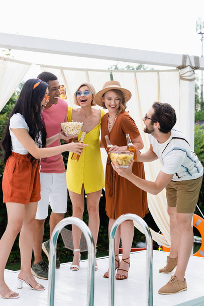Молодой человек предлагает чипсы счастливым многонациональным друзьям во время пивной вечеринки  - Фото, изображение