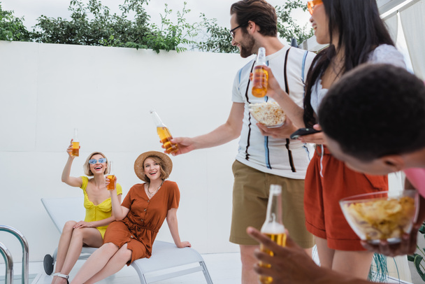 cheerful multicultural friends toasting with bottles of beer during summer party - Photo, image
