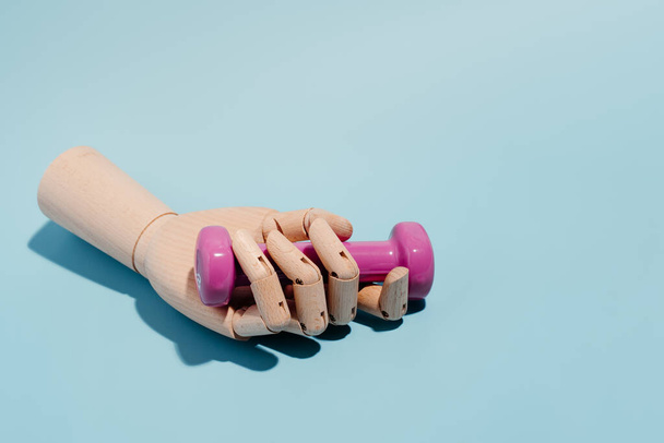 Main en bois avec un haltère rose sur fond bleu. Sport et exercice. - Photo, image