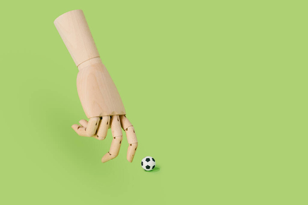 Hand of wood playing with a soccer ball on a green background. football and sport concept. - Foto, Bild