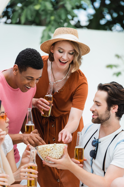 multiethnische Freunde lachen beim Popcornessen während einer Bierparty auf der Terrasse - Foto, Bild