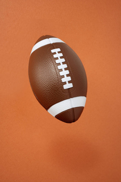 オレンジを背景にしたアメリカンフットボール。スポーツと競争。コピースペース. - 写真・画像