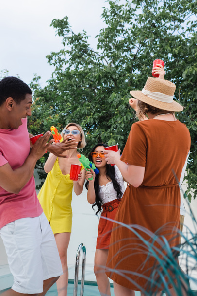 захоплені багатоетнічні друзі розважаються з водяними пістолетами під час літньої вечірки
 - Фото, зображення