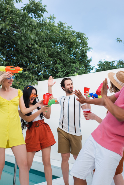 happy interracial friends having fun with water pistols during summer party - Photo, Image