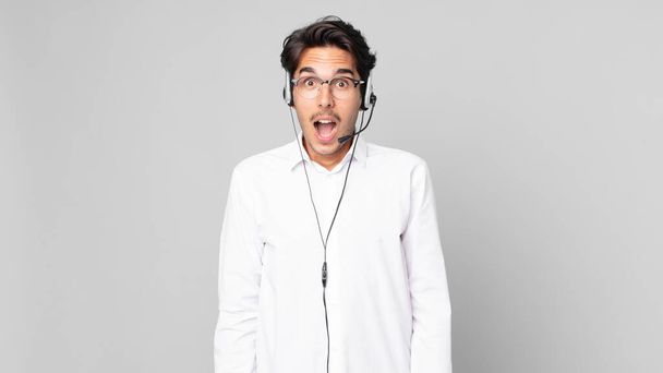 young hispanic man looking very shocked or surprised. telemarketer concept - Fotó, kép