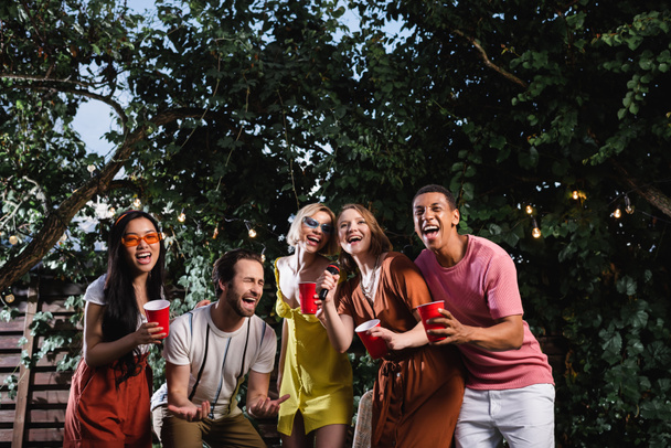 Multikulturelle Freunde mit Drinks singen Karaoke im Freien während der Party  - Foto, Bild
