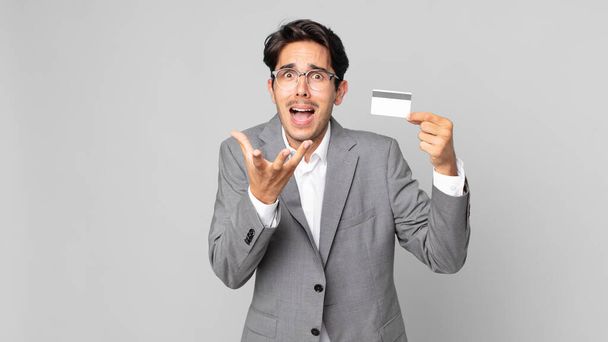 young hispanic man looking desperate, frustrated and stressed and holding a credit card - 写真・画像