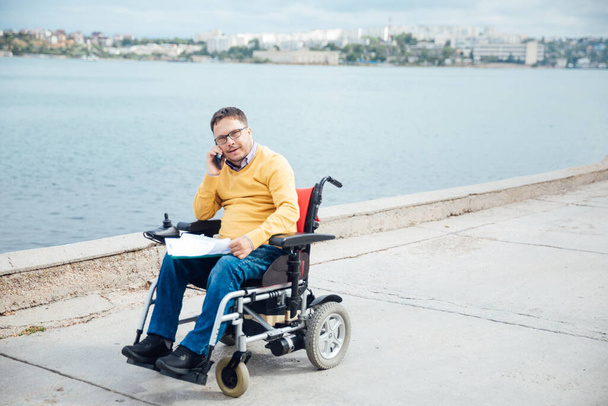 mężczyzna niepełnosprawny na wózku inwalidzkim rozmawiający na smartfonie - Zdjęcie, obraz