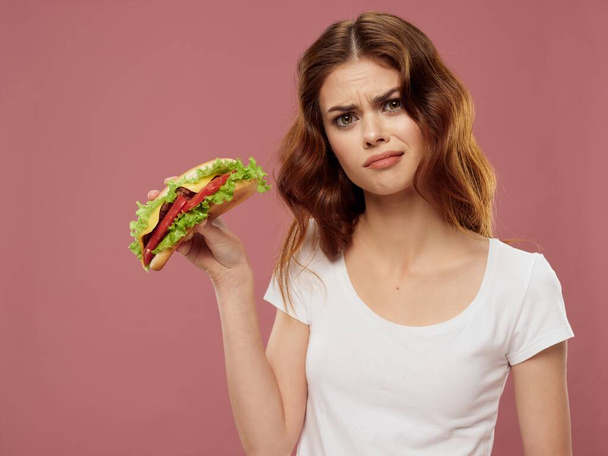 Beyaz tişörtlü kadın hamburger fast food pembe arka plan - Fotoğraf, Görsel