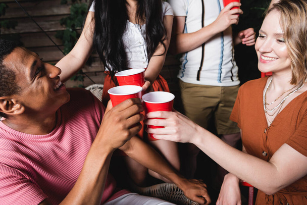 African american man toasting plastic cup with smiling friend during party  - 写真・画像