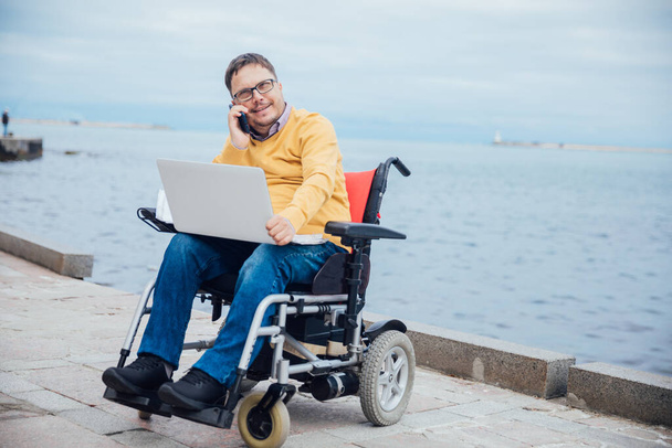Tekerlekli sandalyede engelli bir adam akıllı telefondan konuşuyor. - Fotoğraf, Görsel