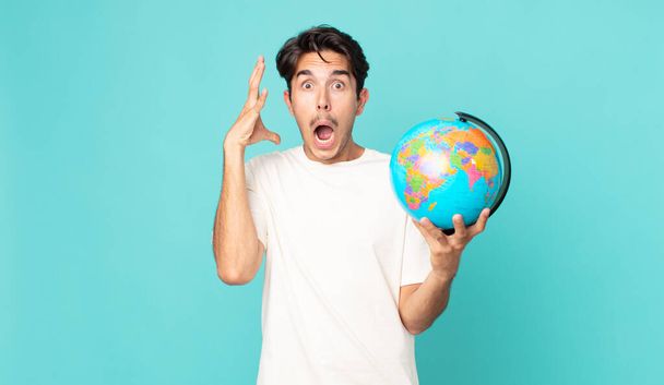 young hispanic man screaming with hands up in the air and holding a world globe map - Foto, immagini