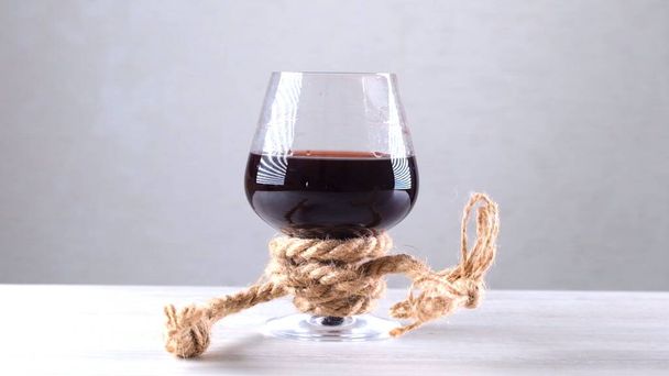 Бокал вина завязан веревкой. Концепция алкогольной зависимости. - Фото, изображение