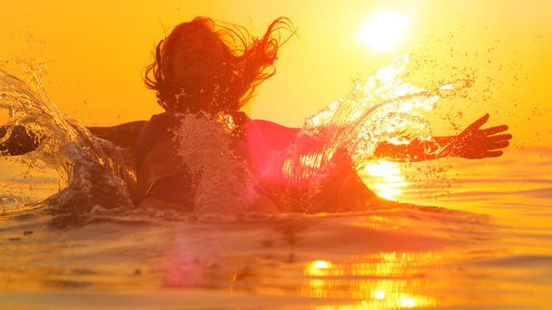 Близко: молодая женщина падает в спокойную океанскую воду с протянутыми руками - Фото, изображение