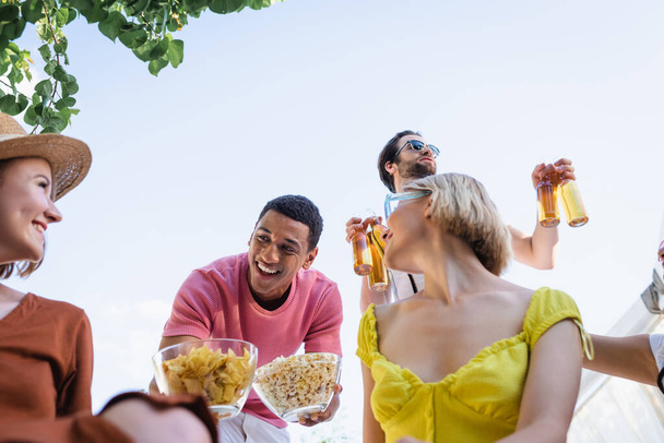 Neşeli, Afro-Amerikan bir adamın açık havada arkadaşlarının yanında atıştırmalık bir şeyler tutması düşük bir bakış açısı.  - Fotoğraf, Görsel