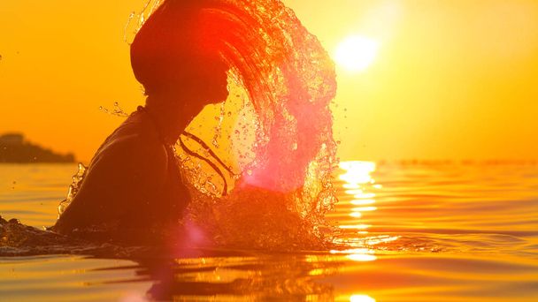 LENS FLARE: Scenic view of a young woman splashing ocean water with her hair. - Foto, Bild