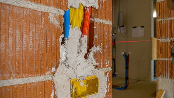 FECHAR UP: argamassa cobrindo condutas coloridas e buraco na parede de tijolo seca lentamente. - Foto, Imagem