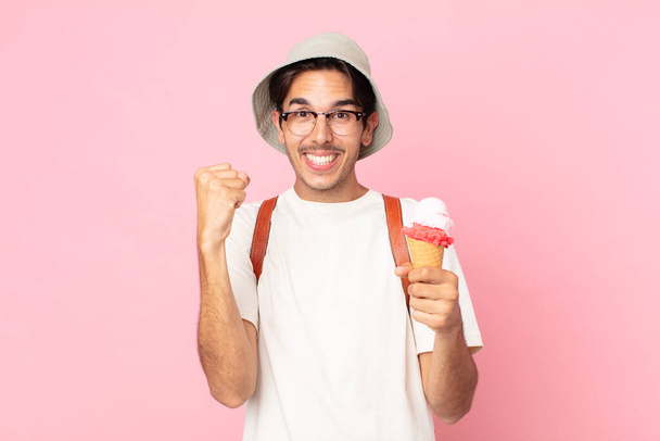 young hispanic man feeling shocked,laughing and celebrating success and holding an ice cream - Foto, Imagem