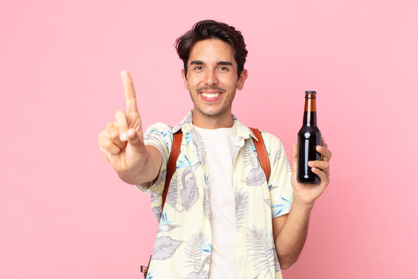young hispanic man smiling proudly and confidently making number one and holding a bottle of beer - Photo, Image