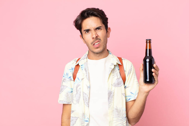 young hispanic man feeling puzzled and confused and holding a bottle of beer - Fotoğraf, Görsel
