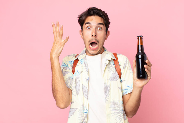 young hispanic man screaming with hands up in the air and holding a bottle of beer - Foto, Imagen