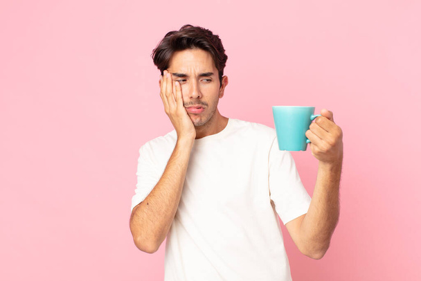 young hispanic man feeling bored, frustrated and sleepy after a tiresome and holding a coffee mug - Foto, immagini
