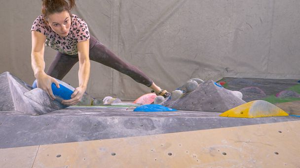 TOP DOWN: Caucasian woman climbs towards the top of an indoor bouldering wall. - Photo, Image
