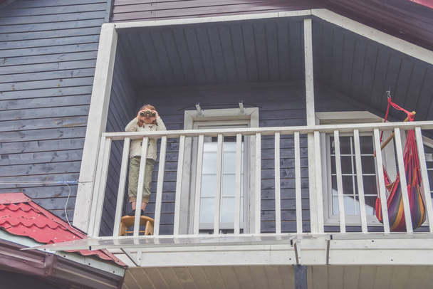 a child girl looks through binoculars standing on the balcony of the house - Foto, Bild