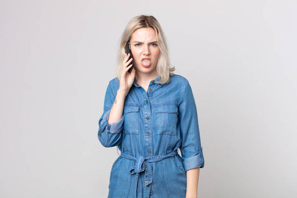 young pretty albino woman feeling disgusted and irritated and tongue out and talking with a smartphone - Foto, imagen