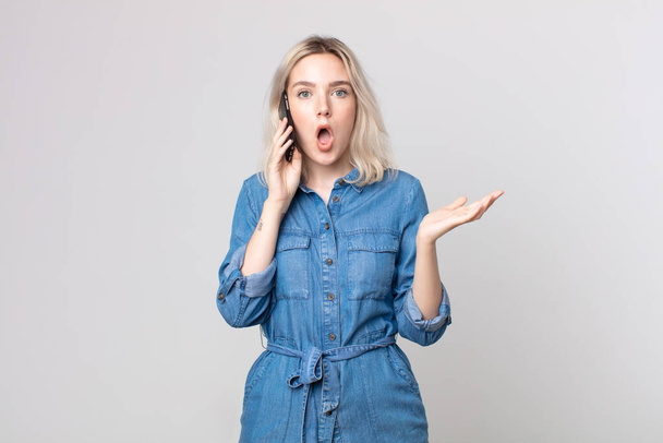 young pretty albino woman feeling extremely shocked and surprised and talking with a smartphone - Foto, imagen