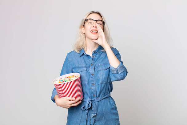 young pretty albino woman feeling happy,giving a big shout out with hands next to mouth with a pop corns bucket - Photo, Image