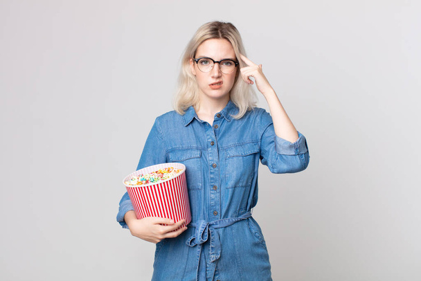 young pretty albino woman feeling confused and puzzled, showing you are insane with a pop corns bucket - Photo, Image