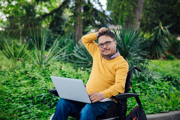 un uomo con disabilità su una sedia a rotelle lavora su un computer su Internet - Foto, immagini