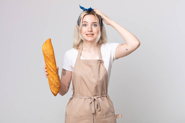 young pretty albino woman feeling stressed, anxious or scared, with hands on head with a bread baguette - Foto, Imagen