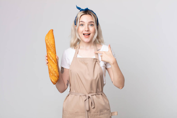 young pretty albino woman feeling happy and pointing to self with an excited with a bread baguette - Fotó, kép