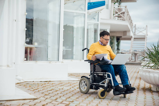 egy kerekesszékes fogyatékkal élő férfi számítógépnél dolgozik az interneten, - Fotó, kép
