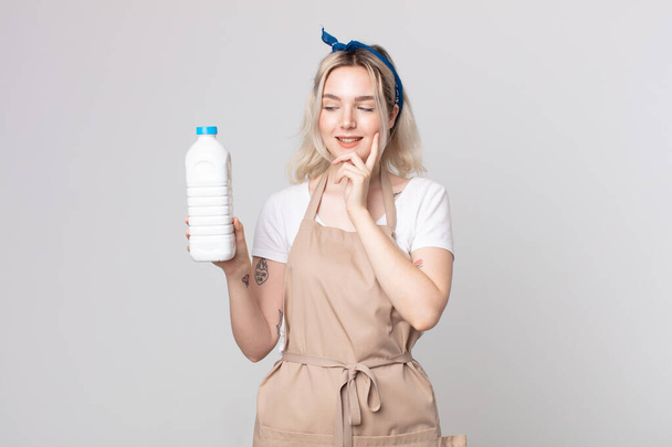 young pretty albino woman smiling with a happy, confident expression with hand on chin with a bottle of milk - Photo, image