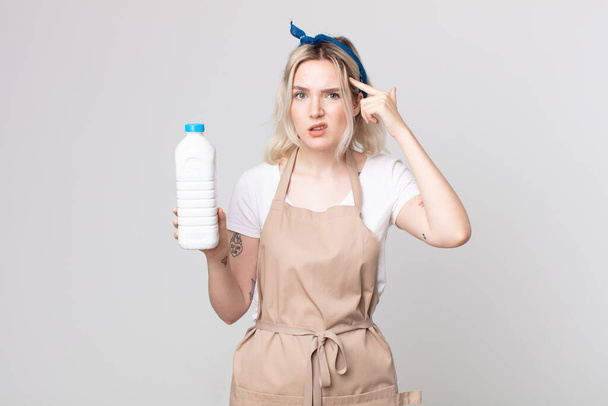 Молодая красивая альбиноса женщина чувствует себя смущенным и озадаченным, показывая, что вы безумны с бутылкой молока - Фото, изображение