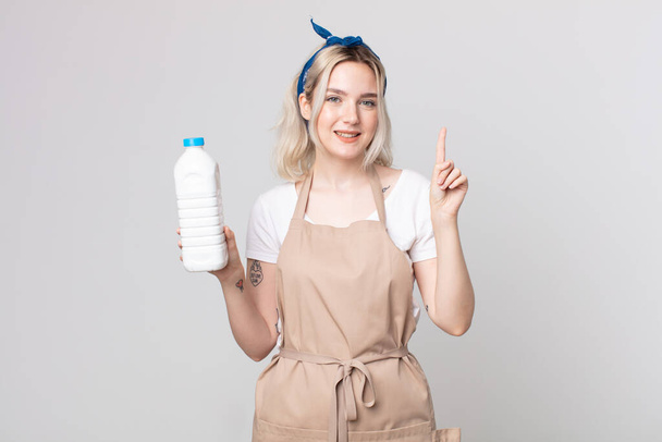 young pretty albino woman smiling and looking friendly, showing number one with a bottle of milk - Photo, image