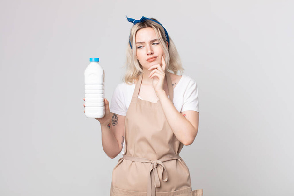 joven bonita mujer albina pensando, sintiéndose dudosa y confundida con una botella de leche - Foto, imagen